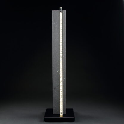 Lampe nommé "Hommage". Modèle lampe à poser de 86 cm, composé d'une colonne de Lave du Mont-Dore et traversé dans la longueur d'une plaque de verre texturé d’où jaillit la lumière. Socle carré en métal thermolaqué de couleur noir. Lampe design et moderne.-Atelier horizon verre