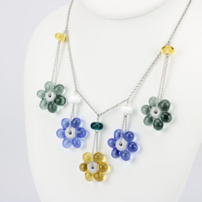 Collier chaine argent 925 avec 5 perles en forme de fleur marguerite de couleur variées, jaune pour celle du milieu puis sur les cotés bleu et grise. Perle fleur transparente. Les perles en verre sont pendantes de part et d'autre de la chaine, tombantes sur le buste. -Atelier horizon verre