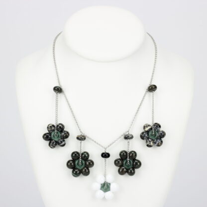 Collier chaine argent 925 avec 5 perles en forme de fleur marguerite de couleur sombre (noir, gris), avec effet marbré noir mais blanche pour celle du milieu. Perles fleur opaque. Les perles en verre sont pendantes de part et d'autre de la chaine, tombantes sur le buste. -Atelier horizon verre