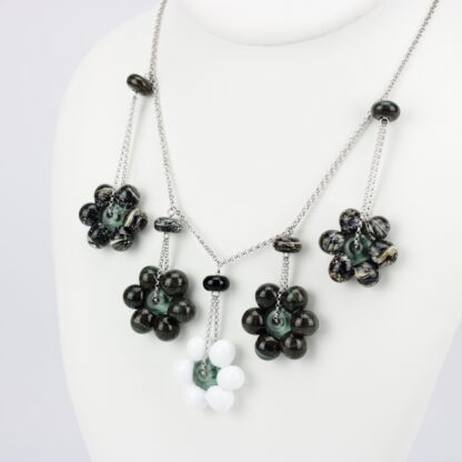 Collier chaine argent 925 avec 5 perles en forme de fleur marguerite de couleur sombre avec effet marbré noir mais blanche pour celle du milieu. Perles fleurs opaque. Les perles en verre sont pendantes de part et d'autre de la chaine, tombantes sur le buste. -Atelier horizon verre