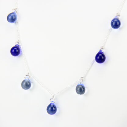 Collier chaine corde en argent 925 avec sept perles de verre aux tons camaïeu de bleu. Collier mi-long avec les gouttes de verre disposées tout autour de la chaîne au niveau du buste. Perles lumineuses et transparentes. -Atelier horizon verre