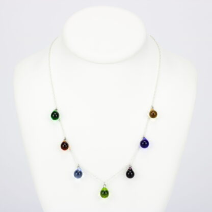 Collier chaine corde en argent 925 avec sept perles de verre aux teintes multiples: vert, bleu, ambre, et violet. Collier mi-long avec les gouttes de verre disposées tout autour de la chaîne au niveau du buste. Perles lumineuses et transparentes. -Atelier horizon verre