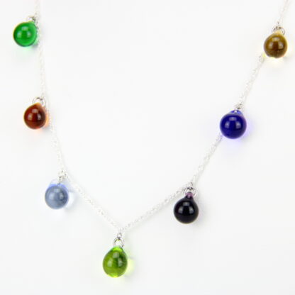 Collier chaine corde en argent 925 avec sept perles de verre aux teintes multiples: vert, bleu, ambre, et violet. Collier mi-long avec les gouttes de verre disposées tout autour de la chaîne au niveau du buste. Perles lumineuses et transparentes. -Atelier horizon verre