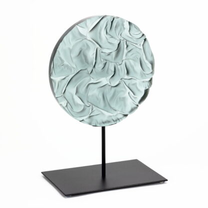 Pièce d'art décoratif de forme circulaire en cristal nommé "Magma" de taille grande (24 cm de diamètre). Objet avec du relief, texturés, avec des effets de drapé. Pièce en cristal de couleur grise sur support en métal thermolaqué noir. Pâte de verre. -Atelier horizon verre