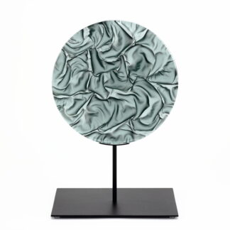 Pièce d'art décoratif de forme circulaire en cristal nommé "Magma" de taille grande (24 cm de diamètre). Objet avec du relief, texturés, avec des effets de drapé. Pièce en cristal de couleur grise sur support en métal thermolaqué noir. Pâte de verre. -Atelier horizon verre