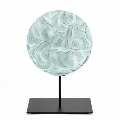 Pièce d'art décoratif de forme circulaire en cristal nommé "Magma" de taille grande (24 cm de diamètre). Objet avec du relief, texturés, avec des effets de drapé. Pièce en cristal de couleur grise sur support en métal thermolaqué noir. Pâte de verre. -Atelier horizon verre