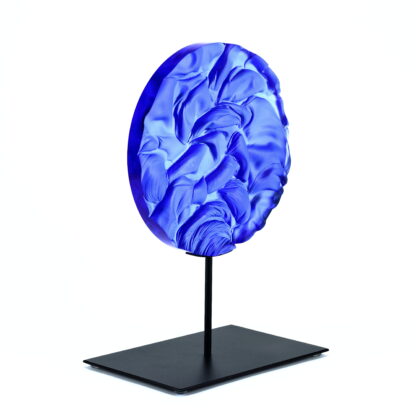 Pièce d'art décoratif de forme circulaire en cristal nommé "Magma" de taille grande (24 cm de diamètre). Objet avec du relief, texturés, avec des effets de drapé. Pièce en cristal de couleur bleu marine sur support en métal thermolaqué noir. Pâte de verre. -Atelier horizon verre