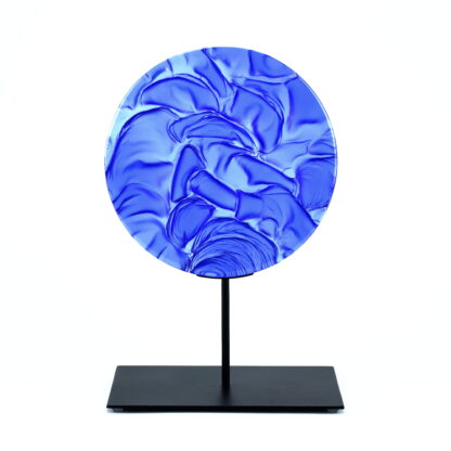 Pièce d'art décoratif de forme circulaire en cristal nommé "Magma" de taille grande (24 cm de diamètre). Objet avec du relief, texturés, avec des effets de drapé. Pièce en cristal de couleur bleu marine sur support en métal thermolaqué noir. Pâte de verre. -Atelier horizon verre