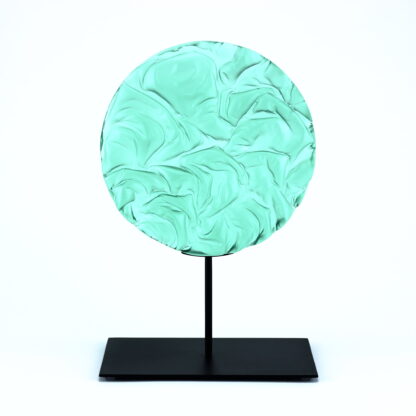 Pièce d'art décoratif de forme circulaire en cristal nommé "Magma" de taille grande (24 cm de diamètre). Objet avec du relief, texturés, avec des effets de drapé. Pièce en cristal de couleur vert menthe sur support en métal thermolaqué noir. Pâte de verre. -Atelier horizon verre