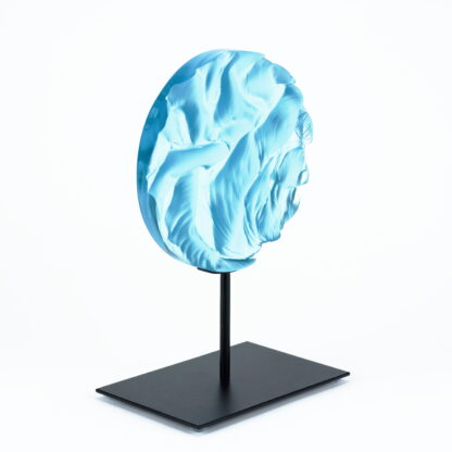 Pièce d'art décoratif de forme circulaire en cristal nommé "Magma" de taille moyenne (18 cm de diamètre). Objet avec du relief, texturés, avec des effets de drapé. Pièce en cristal de couleur bleu ciel sur support en métal thermolaqué noir. Pâte de verre. -Atelier horizon verre