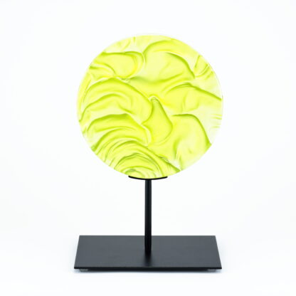 Pièce d'art décoratif de forme circulaire en cristal nommé "Magma" de taille moyenne (18 cm de diamètre). Objet avec du relief, texturés, avec des effets de drapé. Pièce en cristal de couleur jaune citron sur support en métal thermolaqué noir. Pâte de verre. -Atelier horizon verre