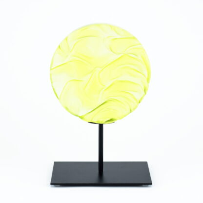 Pièce d'art décoratif de forme circulaire en cristal nommé "Magma" de taille moyenne (18 cm de diamètre). Objet avec du relief, texturés, avec des effets de drapé. Pièce en cristal de couleur jaune citron sur support en métal thermolaqué noir. Pâte de verre. -Atelier horizon verre