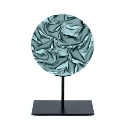 Pièce d'art décoratif de forme circulaire en cristal nommé "Magma" de taille moyenne (18 cm de diamètre). Objet avec du relief, texturés, avec des effets de drapé. Pièce en cristal de couleur gris sur support en métal thermolaqué noir. Pâte de verre. -Atelier horizon verre