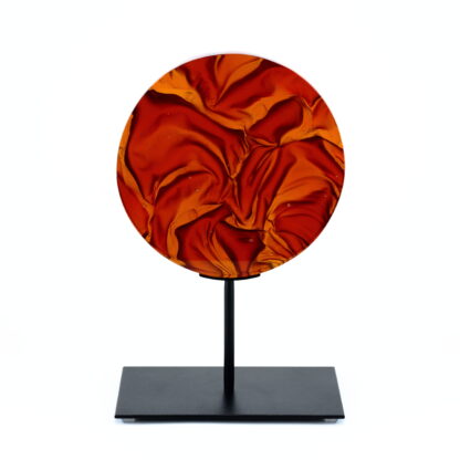 Pièce d'art décoratif de forme circulaire en cristal nommé "Magma" de taille moyenne (18 cm de diamètre). Objet avec du relief, texturés, avec des effets de drapé. Pièce en cristal de couleur rouge sur support en métal thermolaqué noir. Pâte de verre. -Atelier horizon verre