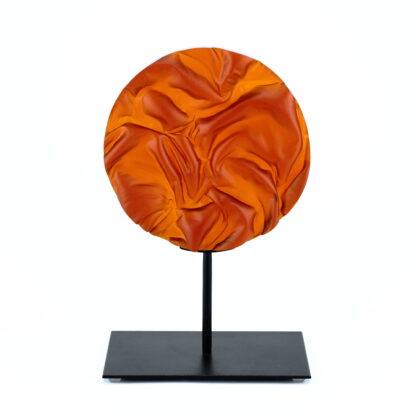 Pièce d'art décoratif de forme circulaire en cristal nommé "Magma" de taille moyenne (18 cm de diamètre). Objet avec du relief, texturés, avec des effets de drapé. Pièce en cristal de couleur rouge sur support en métal thermolaqué noir. Pâte de verre. -Atelier horizon verre